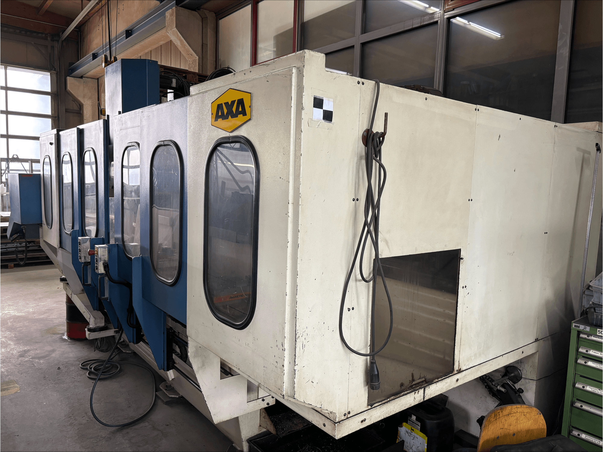 Pionowe centrum obróbcze AXA VSC-1-M/C, widok z przodu, z dużą białą obudową i niebieskim panelem sterowania.