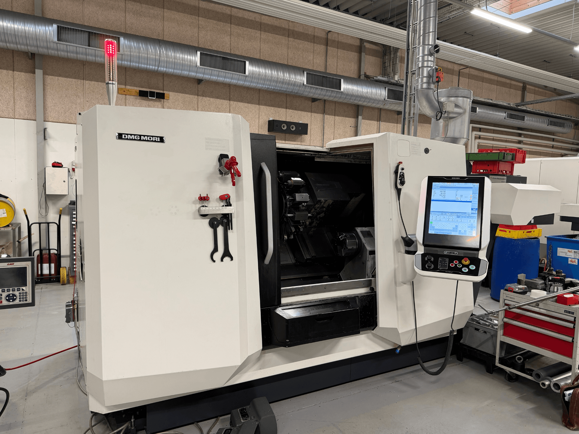 Pozioma tokarka DMG MORI CLX 450 V6 – widok z przodu, na którym widoczny jest panel sterowania, przycisk zatrzymania awaryjnego oraz lampka bezpieczeństwa.