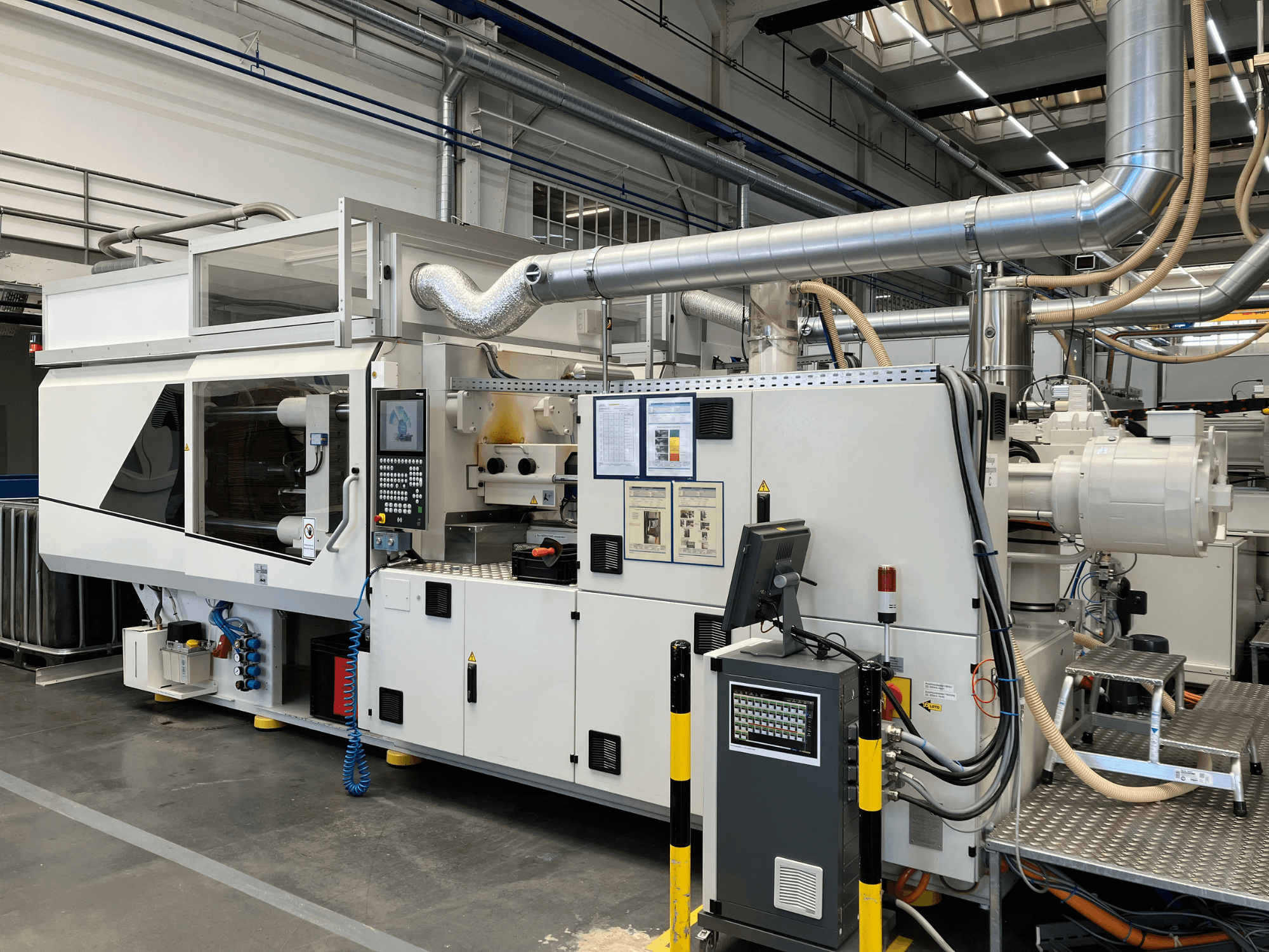 Widok z przodu maszyny przemysłowej z panelem sterowania, rurami i ekranami wyświetlacza, charakteryzującej się eleganckim białym wyglądem i szczegółami technicznymi.