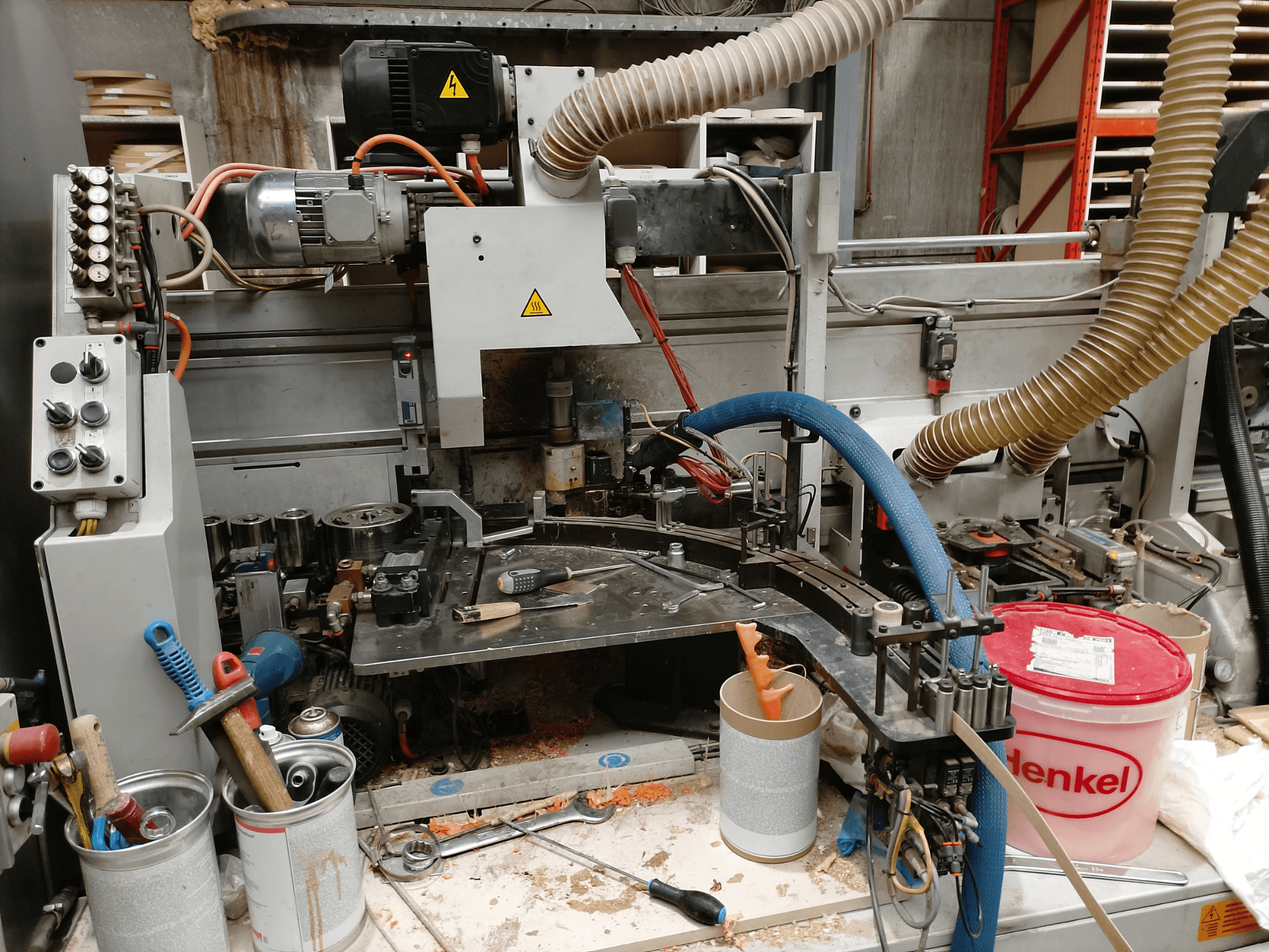 Okleiniarka krawędzi BIESSE Edge Stram B1 w widoku z przodu, prezentująca maszyny, węże i narzędzia robocze wśród wiórów drzewnych.