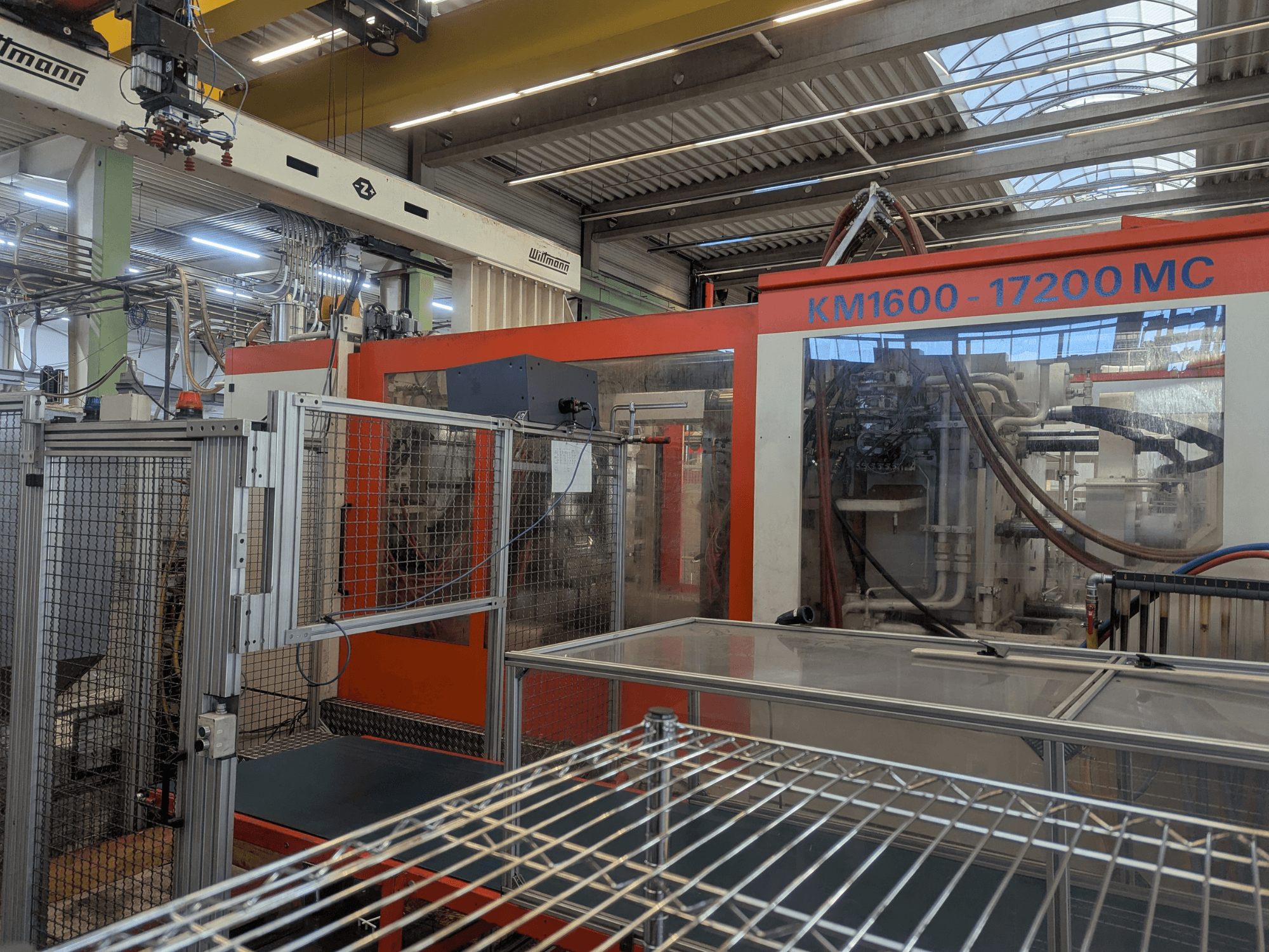 Hydrauliczna wtryskarka Krauss Maffei KM 1600-17200MC, widok z przodu z widocznym panelem sterowania i przewodami hydraulicznymi.