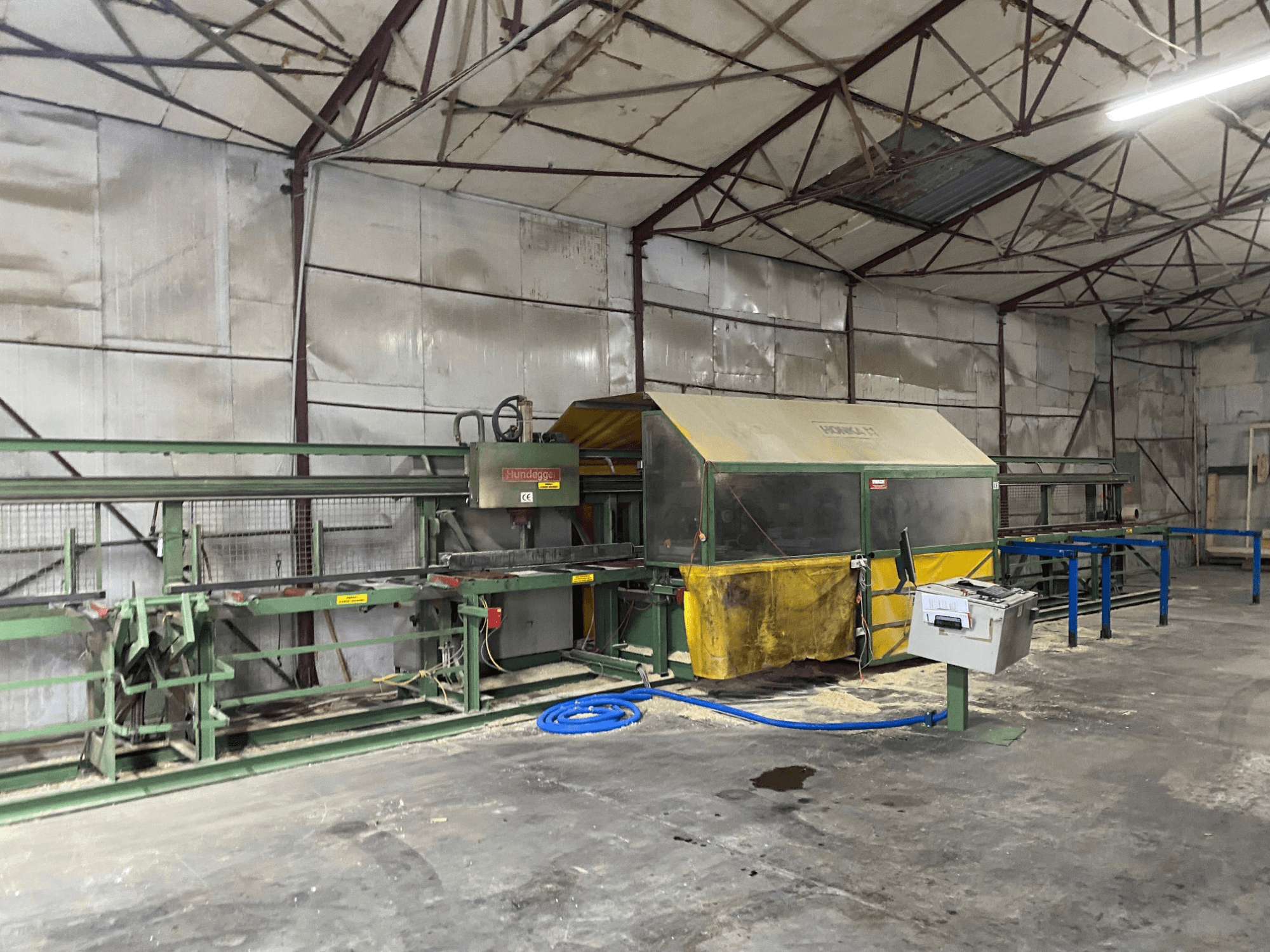 Centrum obróbcze CNC do drewna HUNDEGGER K1 w warsztacie, widok z boku pokazujący maszyny, elementy sterujące i trociny na podłodze.