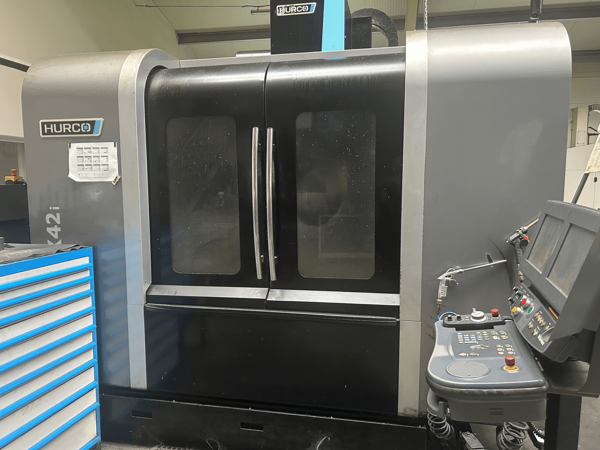 Maszyna CNC Hurco VMX42i, widok z przodu z panelem sterowania z boku, posiada podwójne drzwi i widoczne szczegóły techniczne.