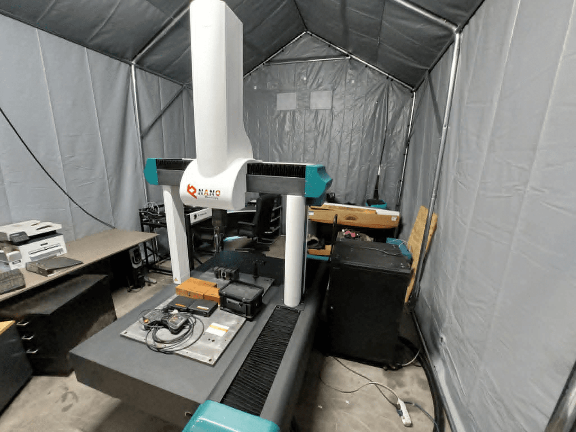 Współrzędnościowa maszyna pomiarowa NANO METROLOGY Micr 7106 w namiocie; widok z przodu pokazujący ramię maszyny i platformę pomiarową z akcesoriami.