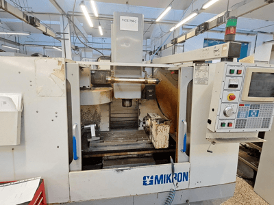 Frezarka CNC Mikron VCE 750-2, widok z przodu, z panelem sterowania i wrzecionem w obszarze obróbki, wykazuje zużycie i zabrudzenia.