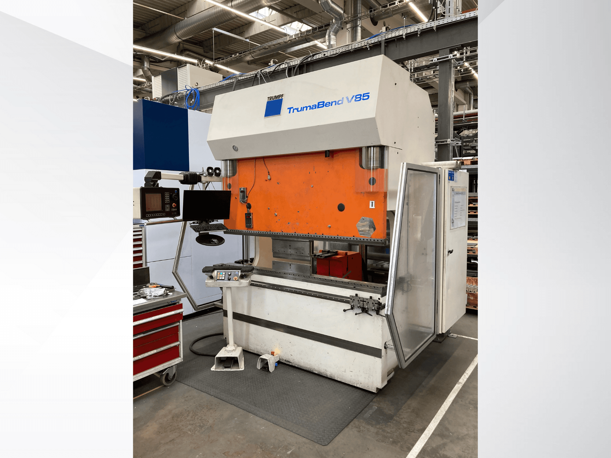 Giętarka TruMatic V85 w fabryce, z pomarańczowym panelem przednim, ekranem sterowania i otwartymi drzwiami bocznymi, widok z boku.