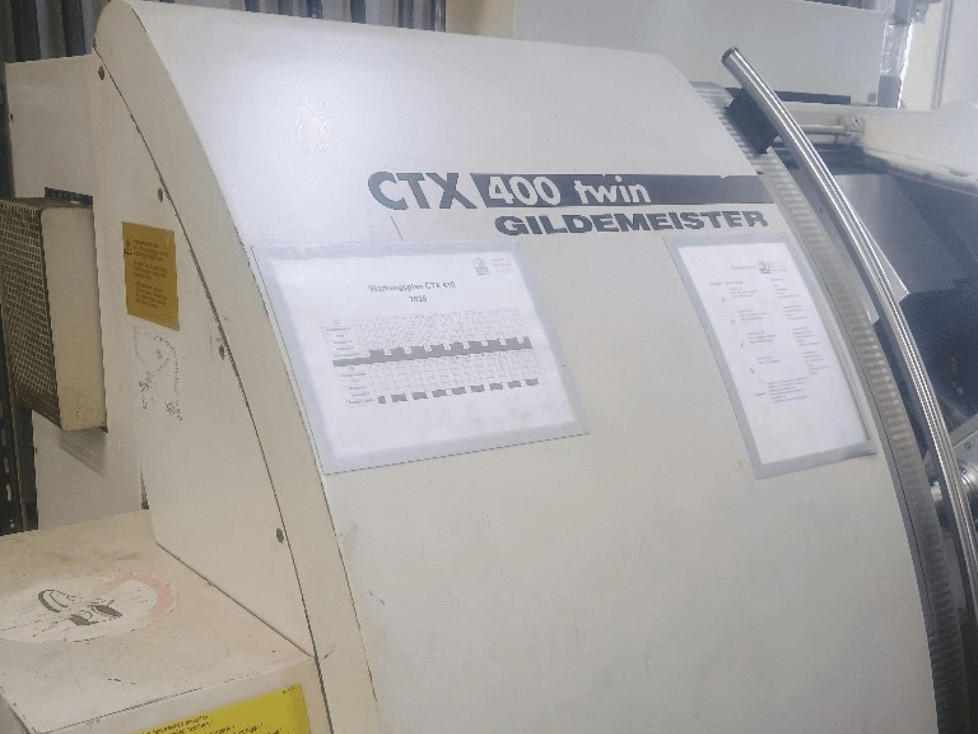 Podwójna tokarka pozioma Gildemeister CTX 400, widok z przodu, przedstawiająca panele sterowania i dokumentację techniczną.