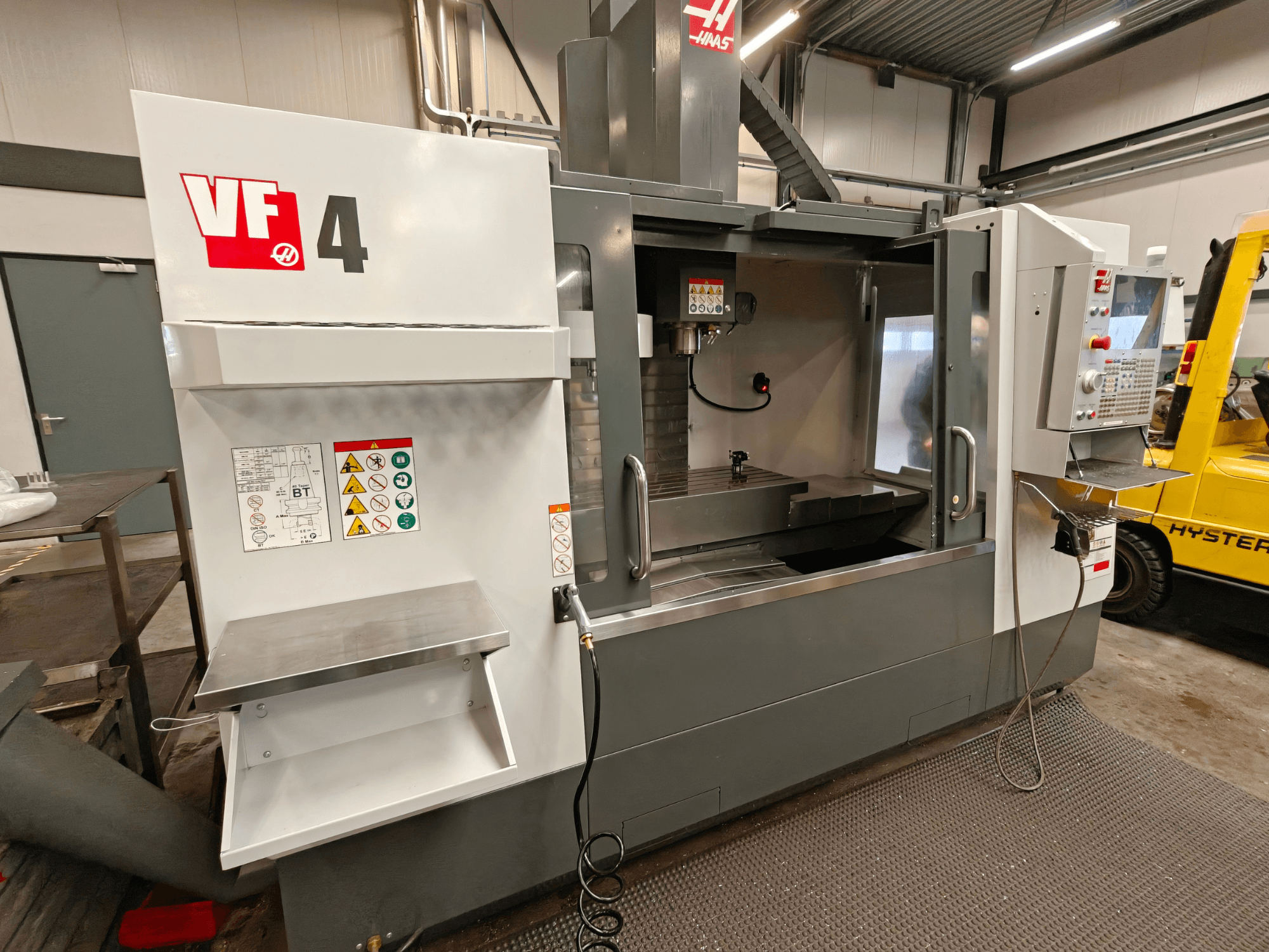 Pionowe centrum obróbcze HAAS VF-4, widok z przodu, z panelem sterowania, obszarem roboczym i etykietami bezpieczeństwa z boku.