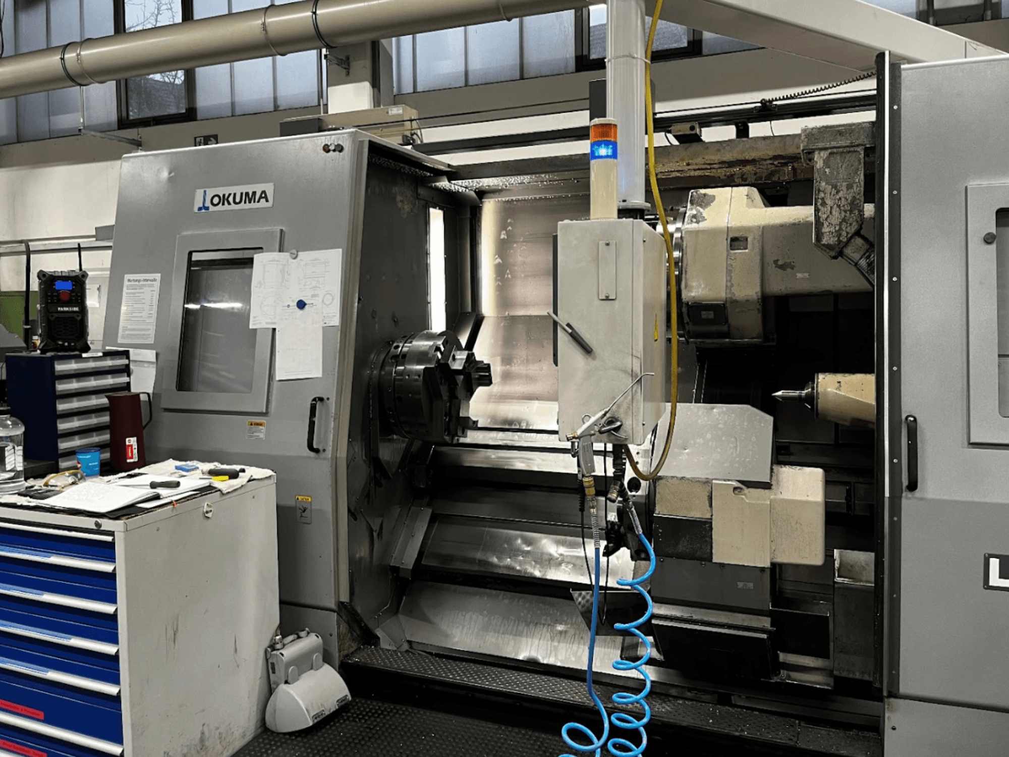 Tokarka pozioma Okuma LU35-M, widok z przodu. Wyposażona w panel sterowania, narzędzia i duży uchwyt do obróbki skrawaniem.