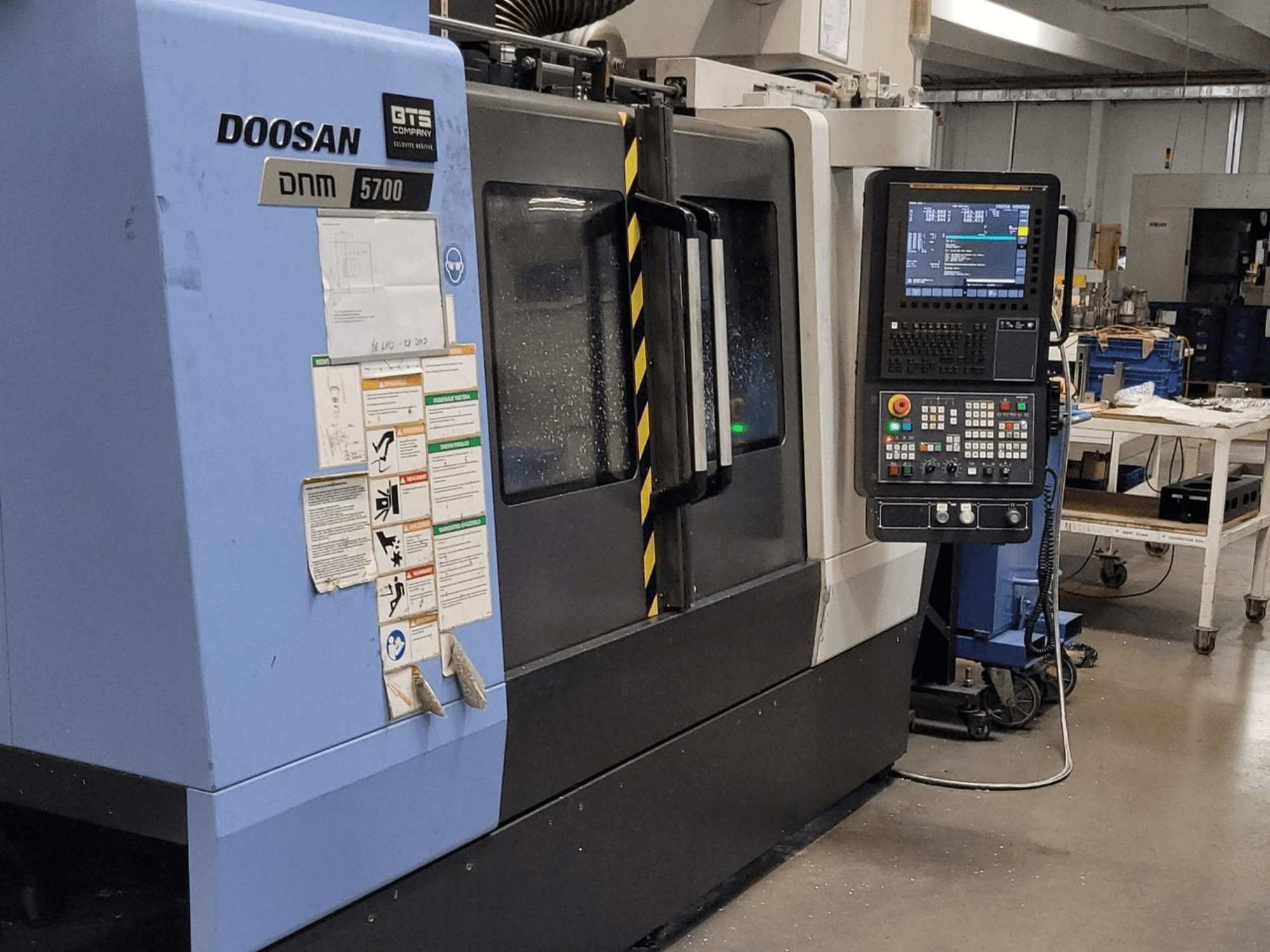 Pionowe centrum obróbcze DOOSAN DNM 5700, widok z przodu, przedstawiający panel sterowania i elementy obsługi.